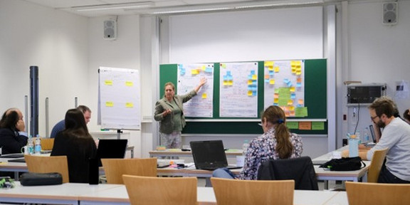 Pictured is the PRAESCO Consortium. Prof. Dr. Frauke Mörike points to posters and leads a discussion in front of a plenary audience.