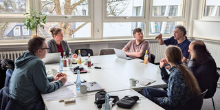 Sechs Personen sitzen an einem Tisch und kollaborieren.