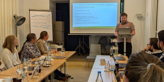 Henrik Sellmann steht vor einem Plenum von PRAESCO-Mitgliederen und hält eine Präsentation.