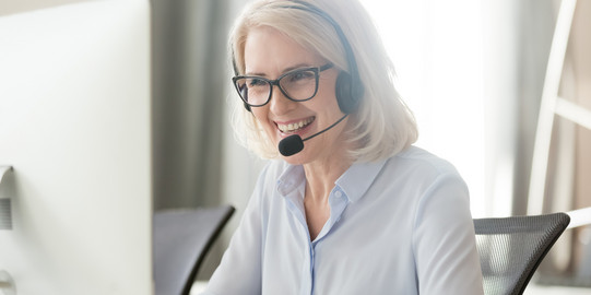 Eine Frau sitzt vor ihrem Laptop und trägt ein Headset. 