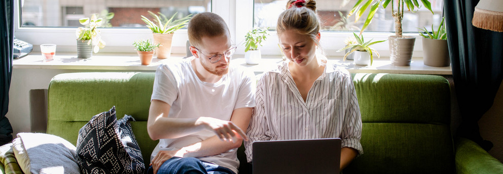 Zwei Studierende arbeiten am Laptop, auf einem Sofa sitzend.